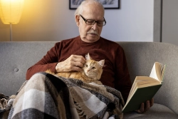 Elderly man reading a book with an orange cat on his lap.
